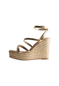 Sandalia cuña dorada con múltiples tiras delgadas. Presenta una base texturizada similar a una cuerda y una parte superior metálica suave. Correa ajustable en el tobillo.