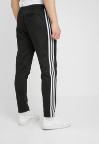 Svart idrottsbyxor med vita sidosträck, smal passform, mjuk textur, med elastisk midja och en liten bakficka.