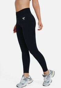 Schwarze High-Waist-Leggings mit glatter Textur und weißem Logo-Akzent. Die Leggings haben eine figurschmeichelnde Passform.