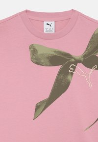 T-shirt en coton rose avec un graphique d'un nœud vert et un logo Puma blanc, avec un col rond et des manches courtes.