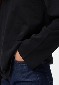 Μαύρο πουκάμισο μακρύ μανίκι από μαλακό βαμβάκι, με άνετη γραμμή και φαρδιά μανίκια, συνδυασμένο με σκούρο μπλε τζιν παντελόνι με ορατές ραφές.