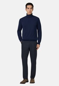 Granatowy sweter z golfem, wykonany z miękkiego materiału, w zestawieniu z ciemnymi spodniami w kratkę i brązowymi zamszowymi butami na sznurowadłach, tworzący schludny wygląd.