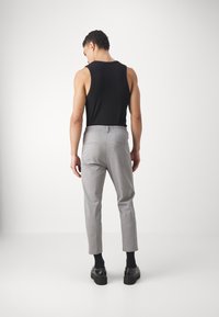 Pantalon gris à coupe décontractée avec une taille élastique, associé à un débardeur noir et des chaussures noires. Tissu lisse, sans motifs visibles.