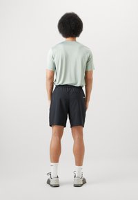 Completo sportivo da uomo composto da una maglietta verde chiaro a maniche corte e pantaloni corti neri con cintura elastica. Visibili calze bianche e scarpe grigie.