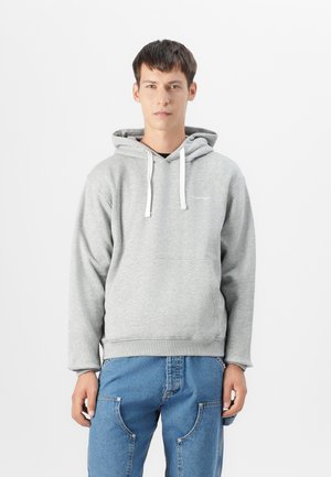Sudadera gris con capucha, cordones blancos, bolsillo delantero y puños acanalados. Combinada con pantalones de mezclilla azul que tienen bolsillos laterales.