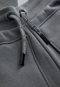 Gray joggers featuring an elastic waistband with drawstrings, textured fabric, side pockets, and subtle branding on the drawstring.