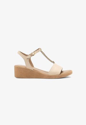 Beżowe sandały na koturnie z teksturowaną korkową podeszwą, regulowanym paskiem na kostce, designem T-bar oraz minimalnymi akcentami metalowymi. Gładkie wykończenie ze skóry.