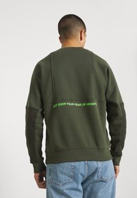 Green sweatshirt with a textured finish, featuring a crew neck and long sleeves. The back has a prominent text in bright green: "GET OVER YOUR FEAR OF HEIGHT."