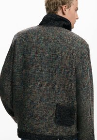 Texturierte, mehrfarbige Jacke mit hohem Kragen, ausgestattet mit einer aufgesetzten Tasche und einem gewobenen Stoffdesign in dunklen und lebhaften Farbtönen.