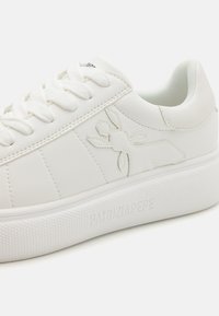 Hvite sneakers med glatt syntetisk overdel, teksturert gummisåle og snøring. Har preget logo og minimalistisk design.