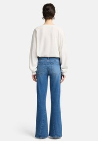 Maglione a maglia crema con spalle scese abbinato a jeans blu a vita alta e a zampa, con tasche posteriori e lavaggio chiaro.