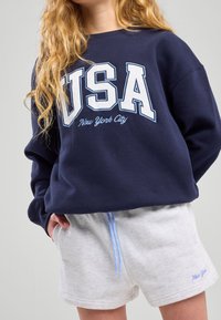 Sweat-shirt navy avec "USA" et "New York City" imprimés en blanc et bleu clair. Shorts gris clair avec cordon bleu et broderie.