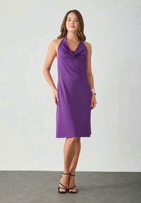 Robe sans manches violette avec un décolleté drapé, design mi-long et tissu lisse. Portée avec des sandales noires à lanières et une montre bracelet.