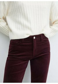 Pantalons en velours côtelé bordeaux avec un devant plat, des poches avant et un bouton en argent. Associés à un pull en crème à rayures texturées.