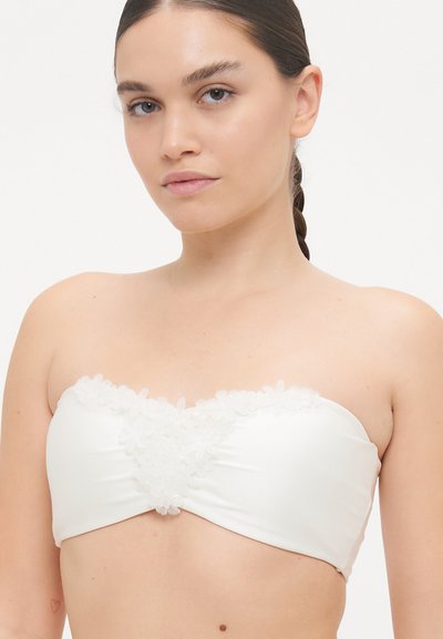 Haut bandeau blanc avec des embellissements floraux à l'avant, fabriqué en tissu lisse avec un design ajusté et sans bretelles.
