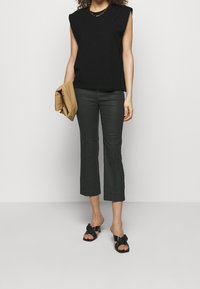 Black sleeveless top, dark cropped pants, and black knotted slide sandals. Holds a tan clutch, featuring smooth materials and a simple design.
