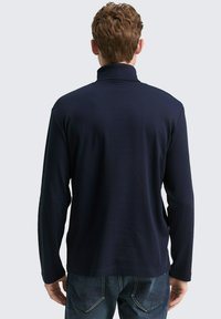 Dunkelblaues Langarmshirt mit Stehkragen, aus einem glatten Stoff gefertigt. Bietet eine legere Passform und eine subtile Textur, kombiniert mit blauen Jeans.