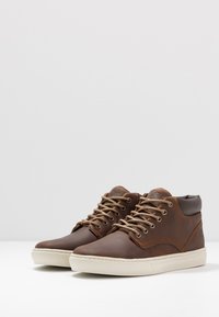 Bruine leren hoge schoenen met lichtbruine veters, een contrasterende beige zool en een minimalistisch ontwerp. Bevat textuuraccenten.
