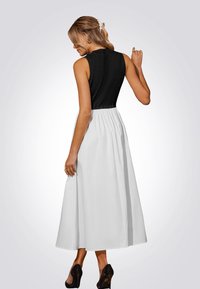 Robe sans manches avec un corsage noir ajusté et une jupe blanche fluide. Présente un haut texturé et une taille froncée. Portée avec des talons noirs.