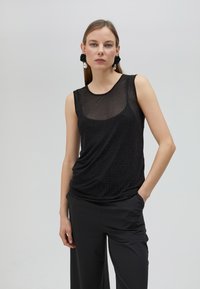 Svart ärmlös topp med en genomskinlig, prickig textur. Draperad design, rund halsringning, kombinerad med vida svarta byxor.