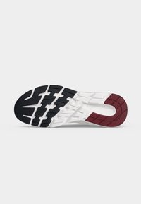 Semelle de chaussure avec des sections noires, blanches et bordeaux et des motifs de grip texturés, présentée sur un fond gris clair uni.
