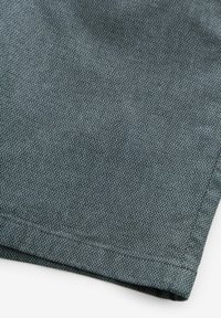 Tissu texturé en bleu canard avec un motif de tissage subtil ; présente un bord replié et une finition de surface lisse.