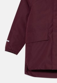 Veste imperméable bordeaux avec des poignets élastiques, un ourlet droit et une grande poche à l'avant. Texture lisse avec un design minimaliste.