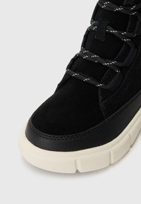 Baskets noires avec une tige en daim et cuir, lacets texturés et une semelle en caoutchouc crème contrastante. Présente un bout rond et des accents de couture.