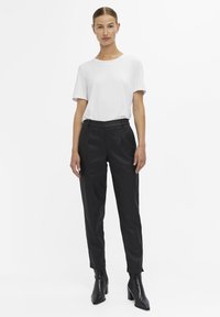 Hvid crewsweater med korte ærmer, parret med sorte skræddersyede bukser med en glat tekstur og tapered ben. Sorte hæle støvler.