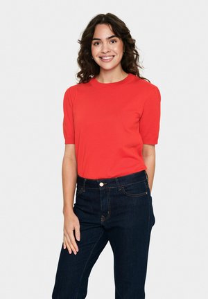 Rotes Kurzarm-Oberteil aus geripptem Stoff mit Rundhalsausschnitt, kombiniert mit dunkelblauen hochtaillierten Jeans. Glatte Textur und enganliegendes Design.