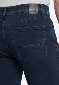 Dunkelblaue Jeans aus Denim, mit einem Leder-Logo-Patch, Gesäßtaschen mit dezentem Stichmuster und slim-fit Design.