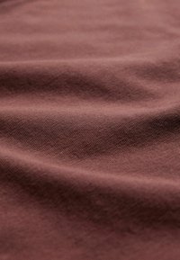 Tissu doux et froissé de couleur mauve atténuée avec une texture lisse et fine et des ombres douces mettant en valeur les plis.