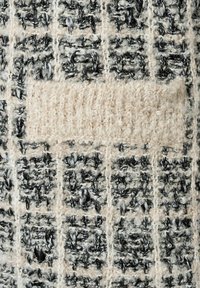 Texturiertes Gewebe mit einem Schwarz-Weiß-Muster, das einen markanten beigen Abschnitt aufweist und eine weiche, flauschige Textur präsentiert.