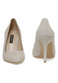 Bežīgas zamšādas augstpapēžu kurpes ar smailu purngalu, izliekta silueta un šauru stiletto papēdi. Zīmols redzams uz iekšējās zoles.
