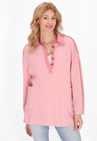 Top henley a maniche lunghe rosa, realizzato in tessuto testurizzato, con due tasche frontali e una patta di bottoni parziale con bottoni marroni.