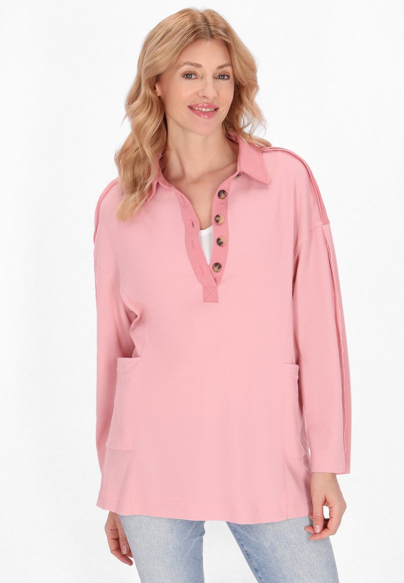 Top henley a maniche lunghe rosa, realizzato in tessuto testurizzato, con due tasche frontali e una patta di bottoni parziale con bottoni marroni.