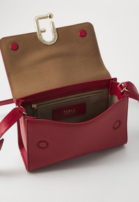 Borsa a mano in pelle rossa con texture liscia, chiusura in hardware dorato e interno khaki dotato di tasca con zip e etichetta del marchio. Tracolla regolabile.