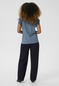 Blusa blu con maniche rifinite in pizzo, abbinata a pantaloni neri a gamba larga e tacchi neri. Tessuto morbido con una vestibilità comoda.