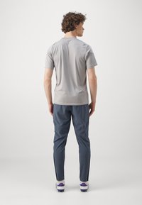 Lysegrå kortærmet skjorte kombineret med mørkeblå tapered bukser. Sættet har en glat tekstur og tætsiddende design, med kontrasterende accenter.