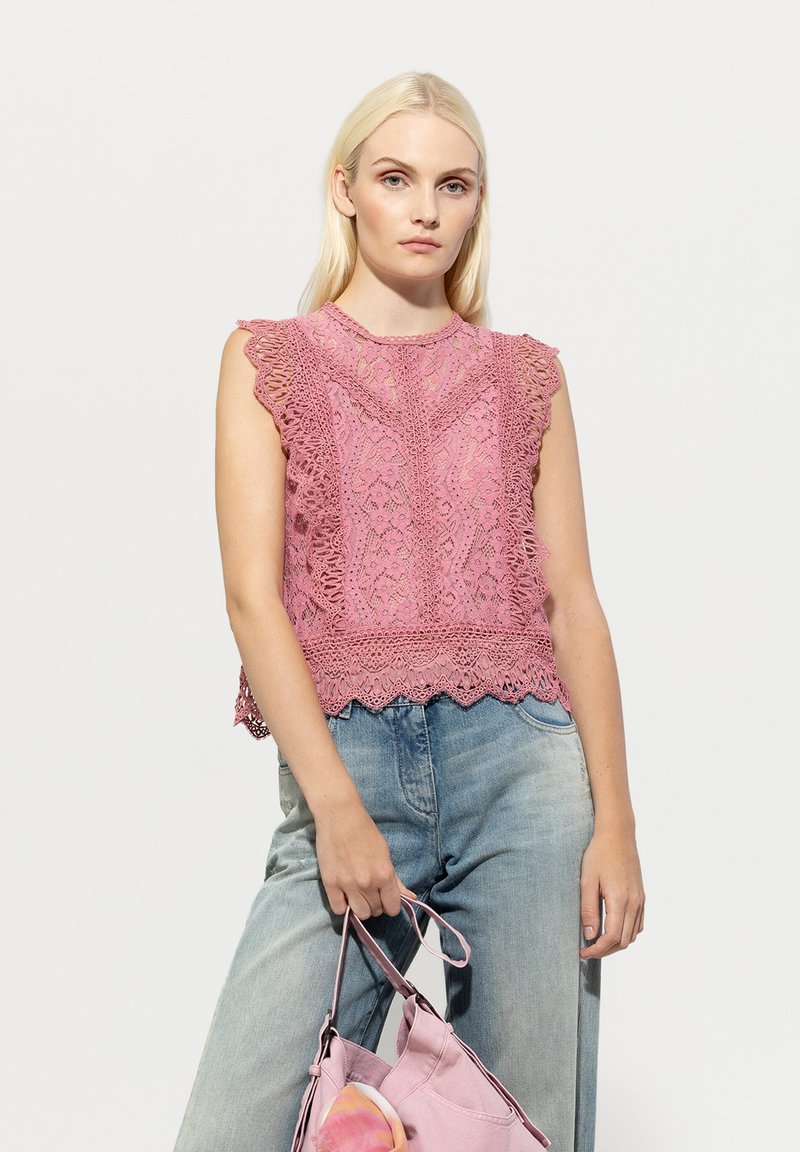 Rosa Spitzenoberteil mit Rüschensleeves, aufwendigen Mustern und einem gewellten Saum, kombiniert mit hellblauen Jeans und einer rosa Tasche.