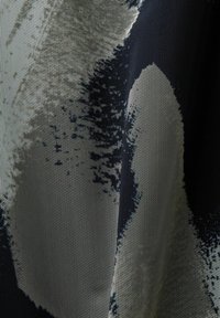 Gros plan sur un tissu à motifs noir et blanc avec un design abstrait texturé et pixellisé, ainsi que de petits détails répétitifs en forme de maille.