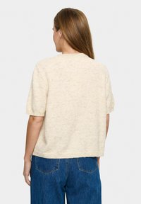 Krémszínű, rövid ujjú kötött pulóver kerek nyakkivágással és puha textúrával, széles lábú kék farmerral párosítva.