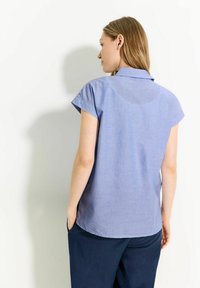 Camicia a maniche corte blu chiaro con colletto, realizzata in tessuto testurizzato, caratterizzata da un orlo curvo, abbinata a pantaloni blu scuro.