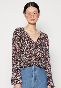 Blusa de manga comprida, decote em V, em preto com um padrão floral. As cores incluem flores rosas, roxas e azuis. Tecido suave, corte descontraído.