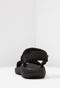 Black sandal featuring a durable textile upper, adjustable straps, and a textured rubber sole for grip. Minimalist design with no patterned accents.