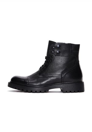 Botas de cuero negras hasta el tobillo con acabado texturizado, punta redonda, diseño con cordones y dos botones a presión en la parte superior. Suela de goma gruesa con relieve.