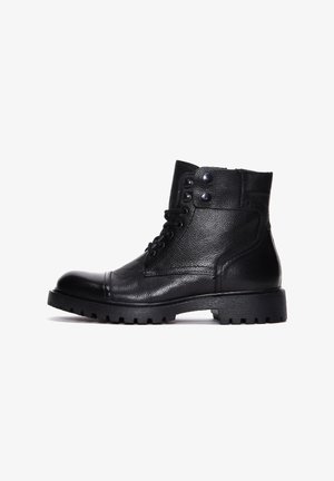 Schwarze Leder-Stiefeletten mit strukturiertem Finish, runder Zehenform, Schnürdesign und zwei Druckknöpfen an der Oberseite. Dicke gummierte Sohle mit Profil.