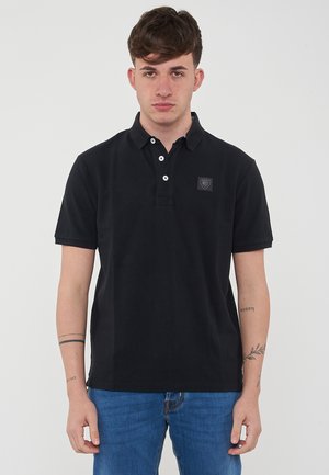 Polo nero in cotone, dotato di colletto con tre bottoni, maniche corte e una piccola toppa con logo sul petto.