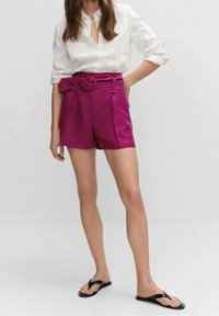 Fuchsia-hohe Shorts mit einem Gürtel-Detail. Hergestellt aus einem strukturierten Stoff, mit Falten und einer lockeren Passform, kombiniert mit einer weißen Bluse.