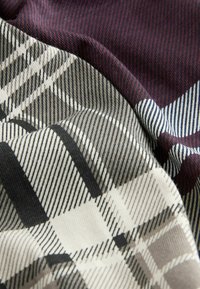 Woven fabric featuring a mix of plaid patterns in shades of maroon, black, beige, and navy, with varied textures and diagonal lines.